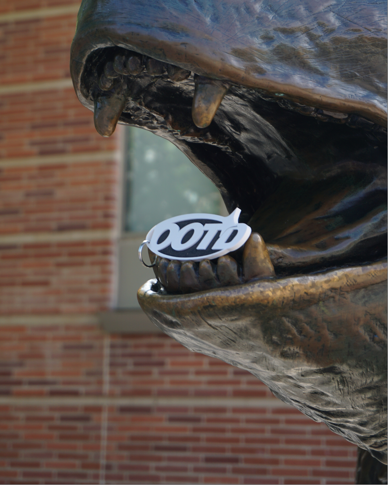 Close-up of a bear statue's mouth with an OOTD Backpack Charm, against a brick building background.